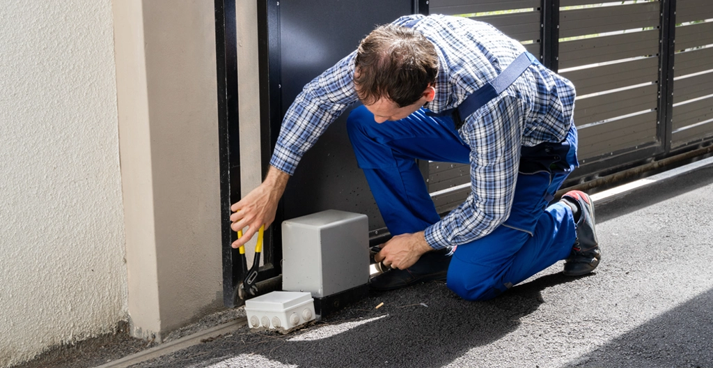 Artisan mesurant le dénivelé avec un niveau laser devant un pilier de portail